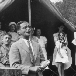 American composer Irving Berlin sings his song "God Bless America" in front of Boy Scouts troop members and spectators gathered at a tent in Monticello, New York in 1940. Instead of collecting royalties from "God Bless America," Berlin created a fund that collected and distributed them to the Boy and Girl Scouts.